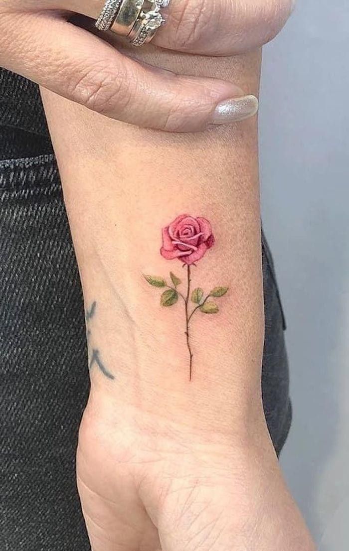 a woman's wrist with a small pink rose tattoo on the left side of her arm