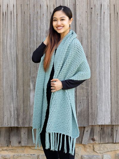 a woman standing in front of a wooden fence wearing a blue knitted shawl