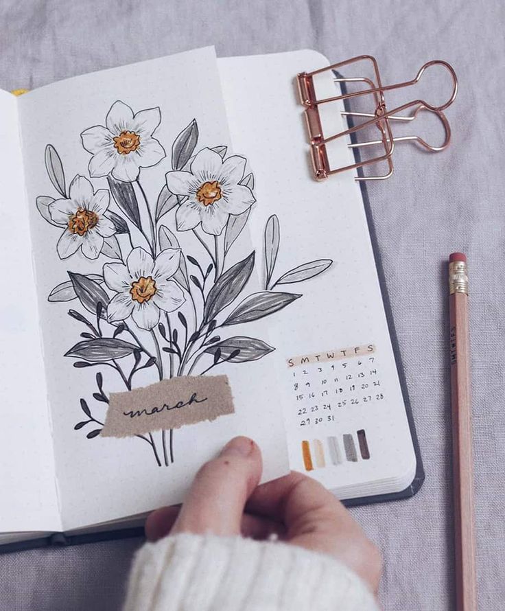 an open notebook with flowers drawn on it next to a pencil and some other items