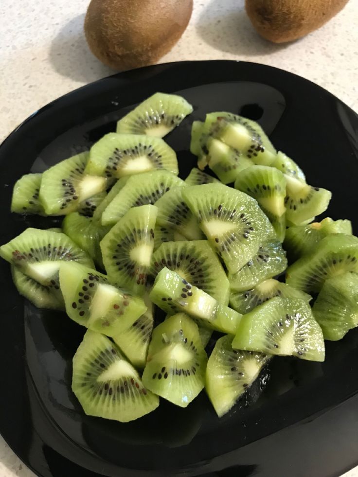 sliced kiwis on a black plate next to two kiwis sitting on a counter