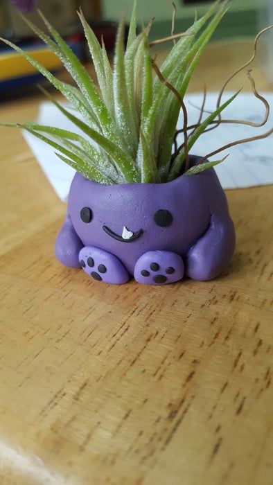 a small purple planter with an adorable face on it's side sitting on a wooden table