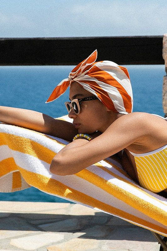 a woman laying on top of a yellow and white striped towel next to the ocean