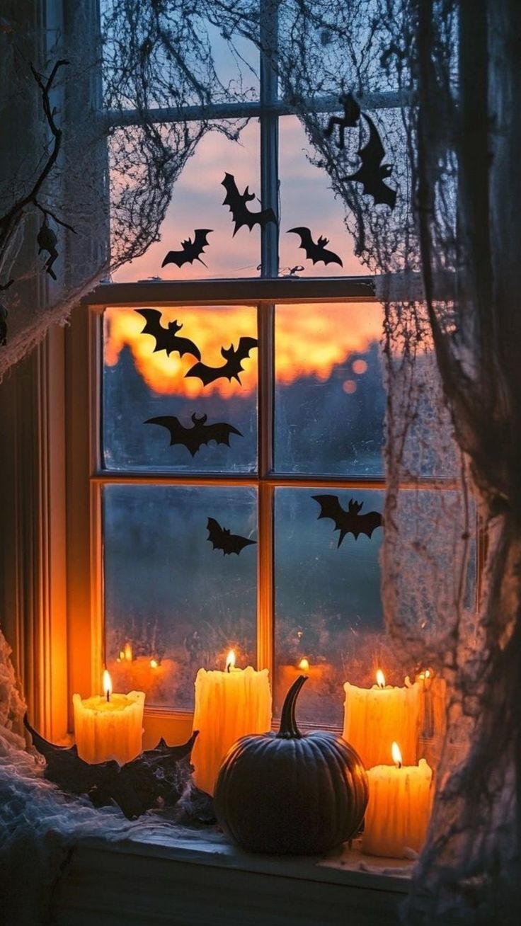 candles are lit in front of a window decorated with bats and pumpkins at night