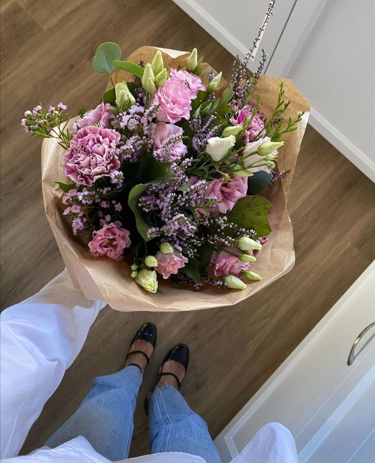 a woman holding a bouquet of flowers on top of a wooden floor next to her feet