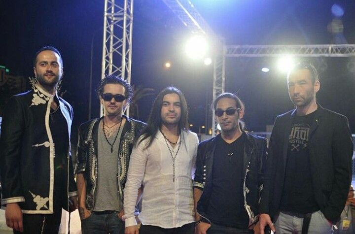 five men standing in front of a stage with lights on and one man wearing sunglasses