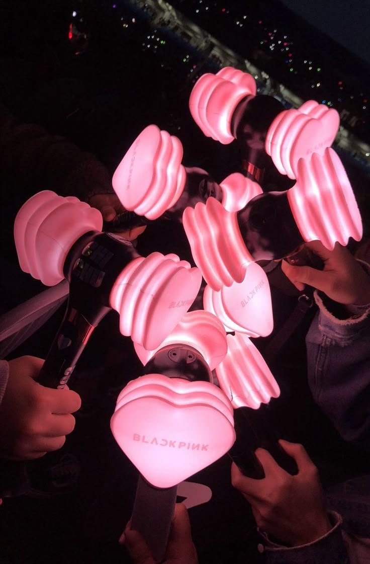 several pink lights are being held up in the air by people holding cell phones and looking at them