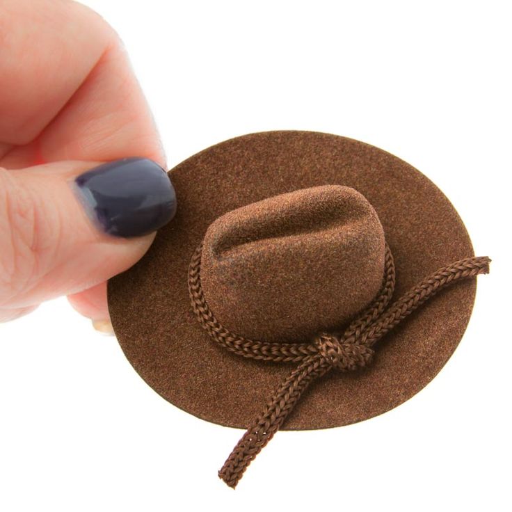 a hand holding a brown hat on top of a white surface with a string attached to it