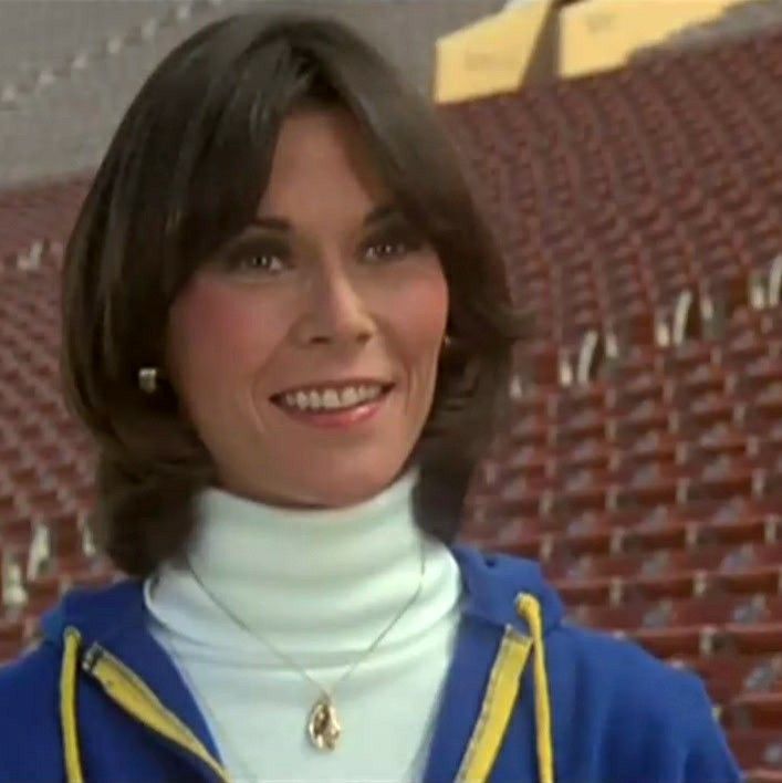 a woman wearing a blue and yellow jacket standing in front of an empty bleachers