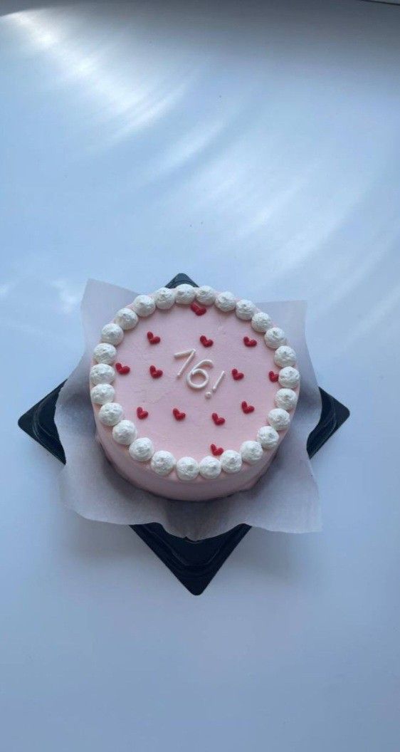 a pink cake with white frosting and red hearts on it sitting on top of a piece of paper