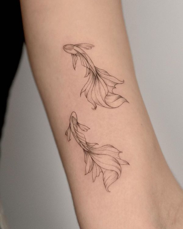 a woman's arm with two goldfish tattoos on the left side of her body