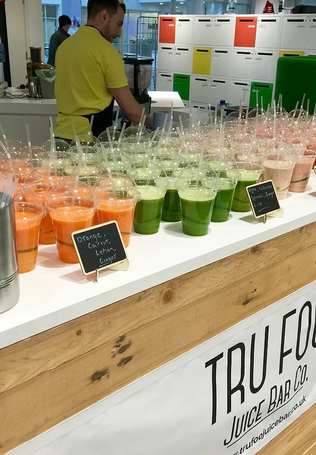 there are many drinks on the table at this juice bar that is filled with orange, green and pink liquids