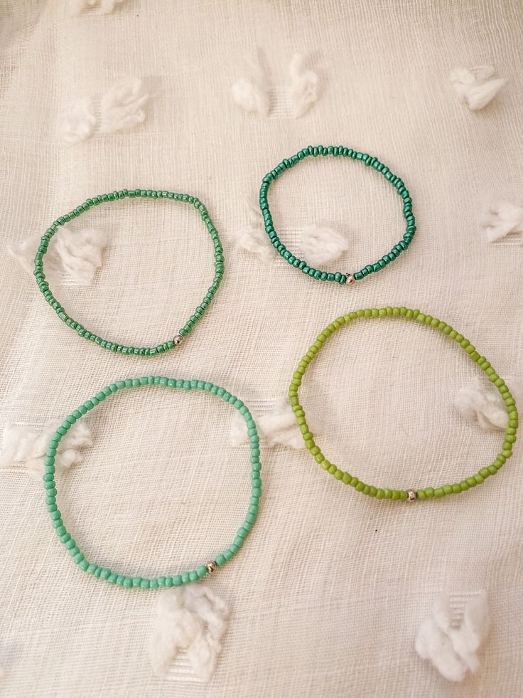 three bracelets with green beads on a white cloth