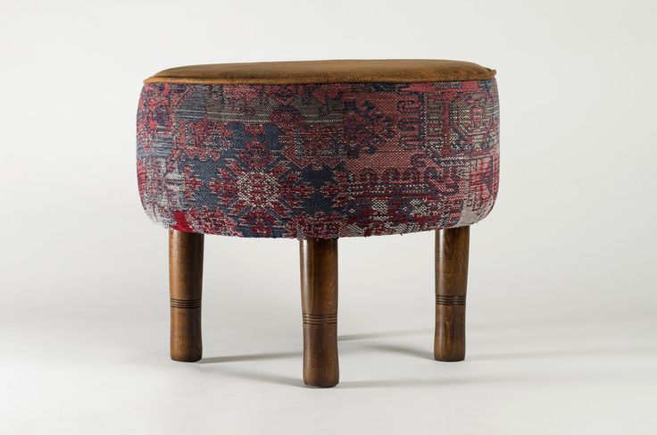 an old stool with wooden legs and a colorful upholstered design on the top