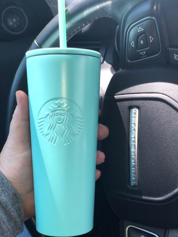 a person is holding a starbucks cup in their hand and steering wheel behind the car