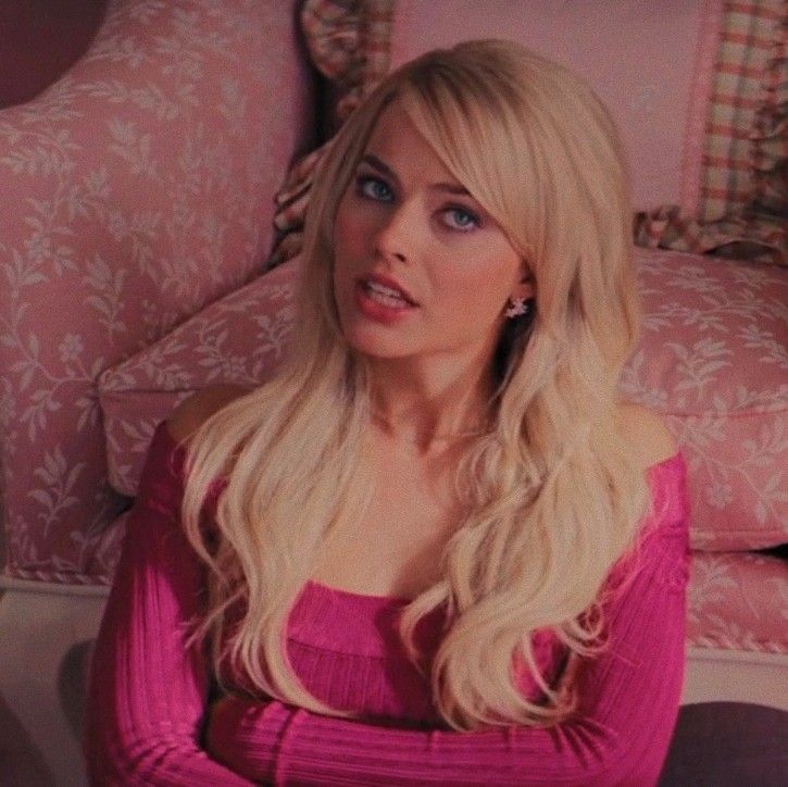 a woman with long blonde hair sitting in front of a pink couch and looking off to the side