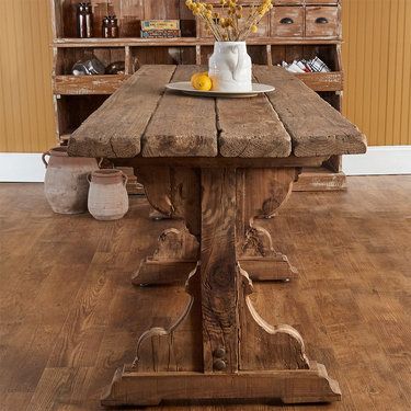 a wooden table with some flowers in a vase on it and an empty plate sitting on top