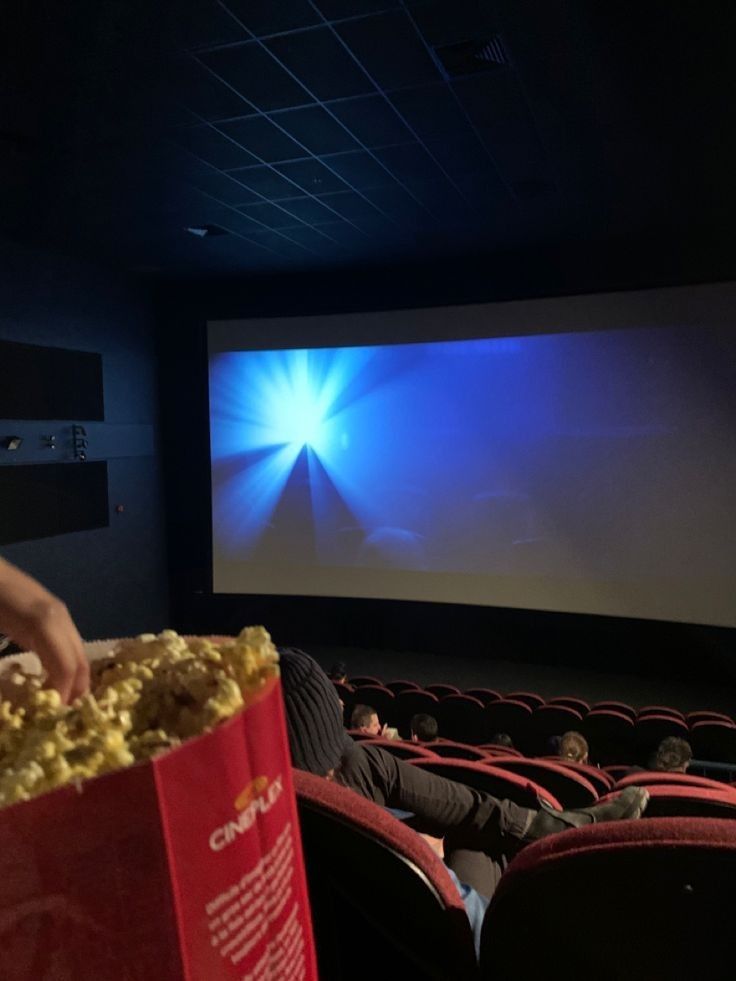 people sitting in chairs watching a movie on the screen and holding popcorn bags with their hands