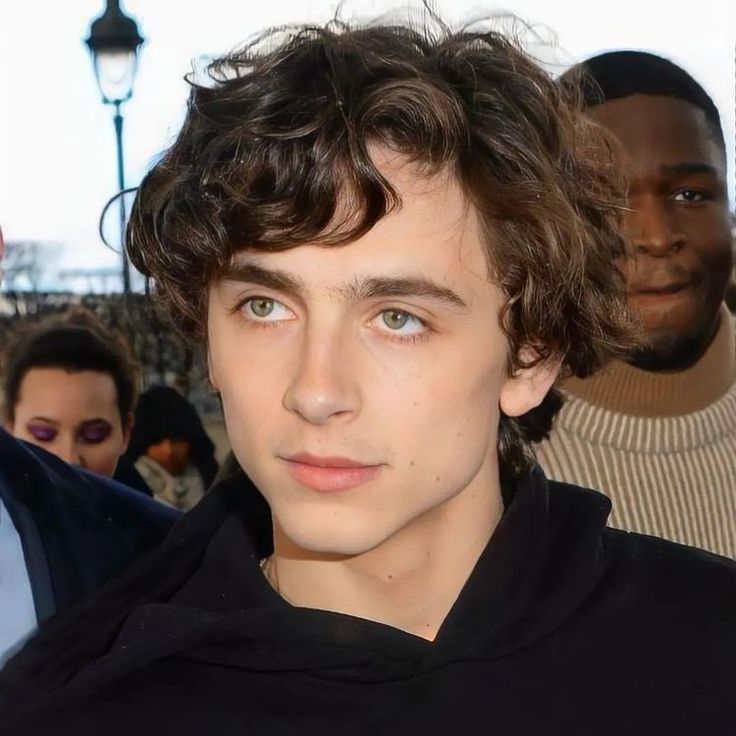 a young man with curly hair standing in front of other men and looking at the camera