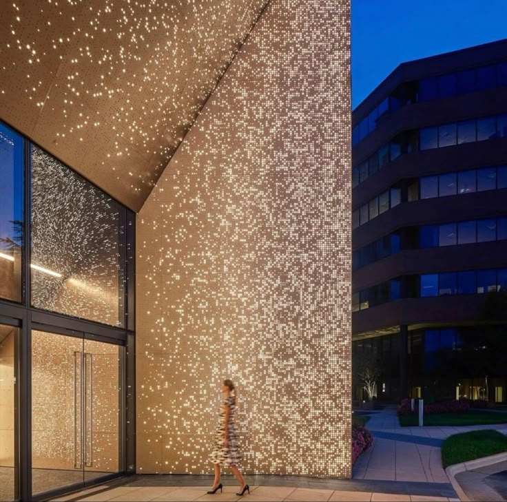 a woman walking past a tall building with lots of lights on it's side