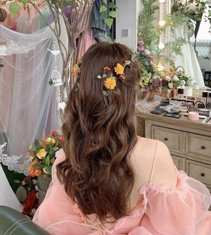 a woman sitting in front of a mirror with flowers on her hair and wearing a pink dress