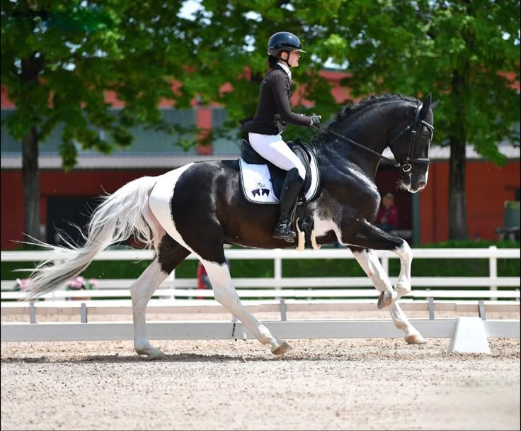 a woman riding on the back of a black and white horse in an arena with trees