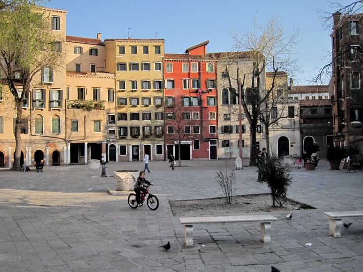 a person riding a bike in the middle of a courtyard with benches and buildings behind them