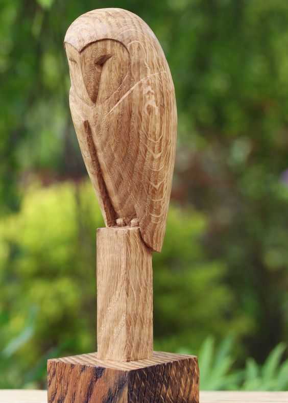 a wooden owl statue sitting on top of a wooden block in front of some trees