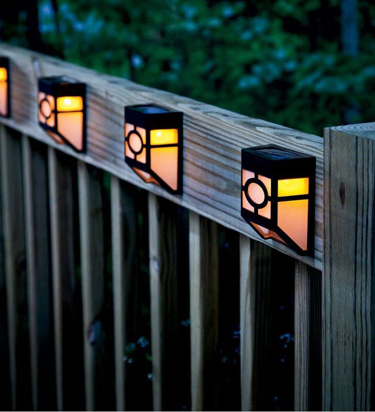 three lights that are on the side of a wooden fence with trees in the background