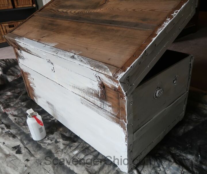 an old chest with some paint on it and a bottle next to it in the corner