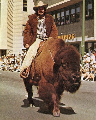 a man riding on the back of a buffalo down a street in front of a crowd