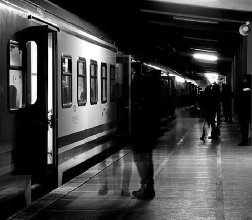 black and white photograph of people standing on the platform next to a train at night