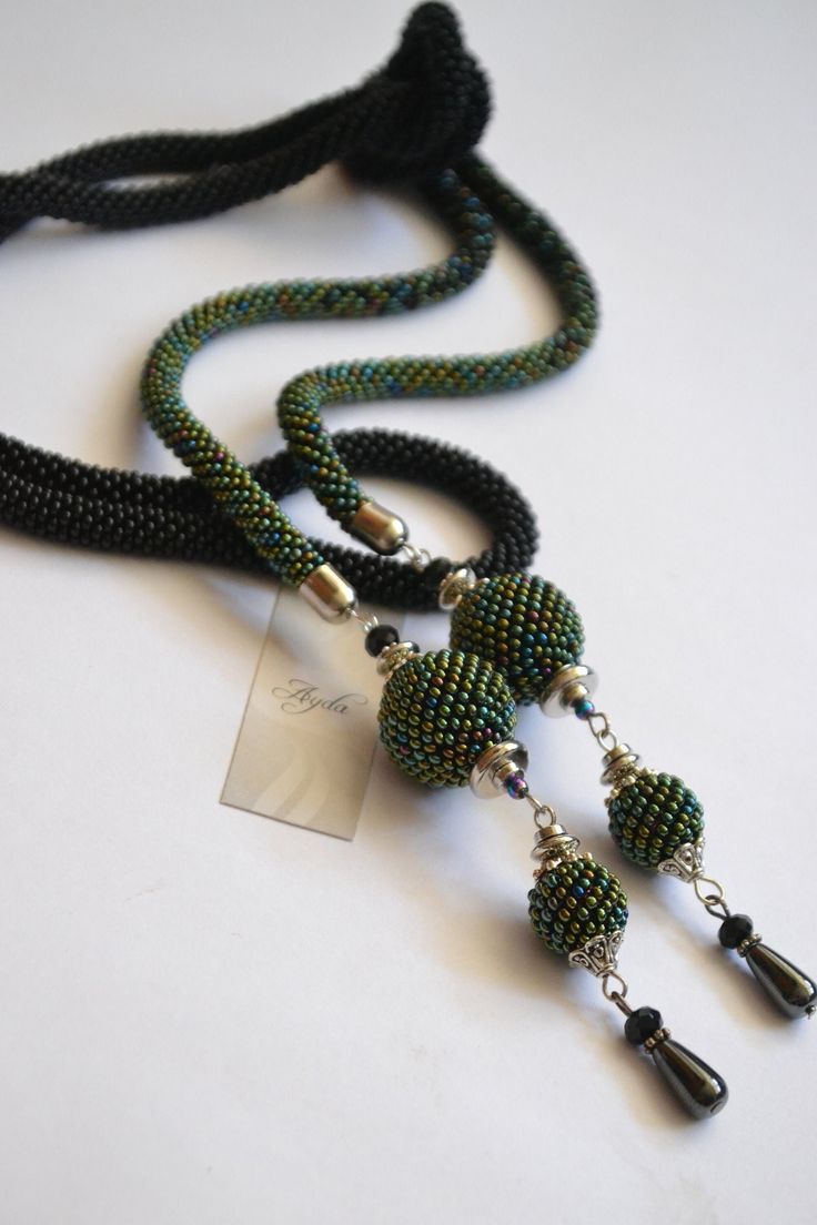 a black and green beaded necklace on a white surface with a tag hanging from it