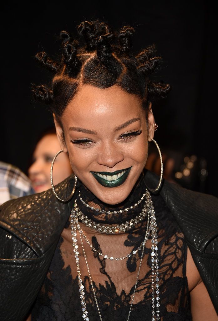 a woman with black makeup and green eyeshade smiles while wearing statement necklaces