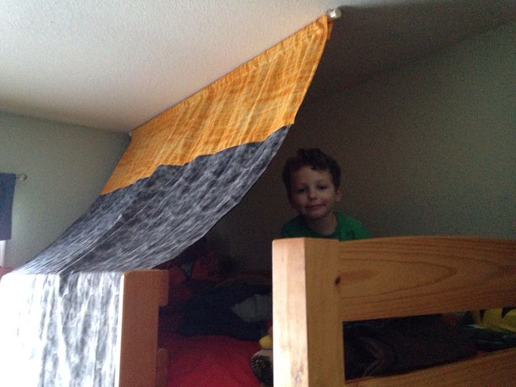 a young boy standing on top of a wooden bunk bed under a tarp over his head