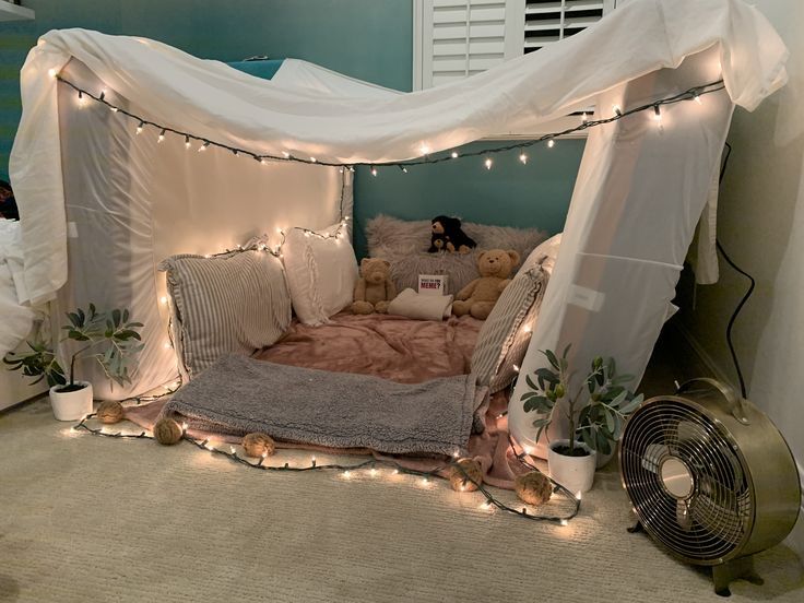 a canopy bed with lights on the ceiling and stuffed teddy bears in pillows under it