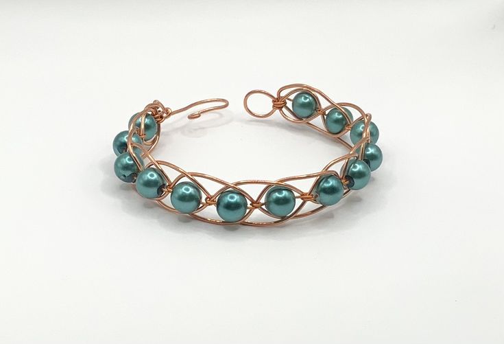 a bracelet with pearls and copper wire on a white surface, the beads are blue