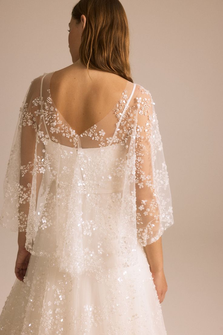 a woman in a white wedding dress with sheer sleeves and beading on the back