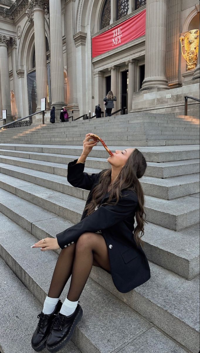 a woman is sitting on the steps drinking from a bottle in front of a building