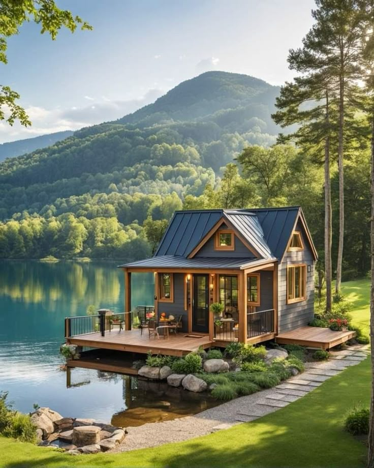 a small house on the shore of a lake with mountains and trees in the background