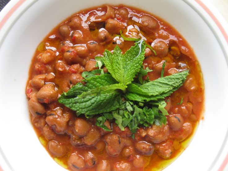 a white bowl filled with beans and green garnish on top of a table