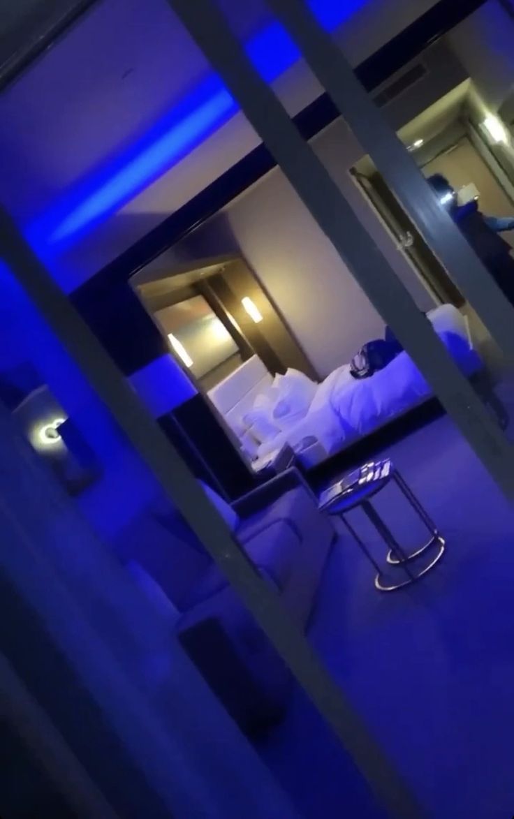 a bedroom with blue lighting and a bed in the background is seen through glass doors