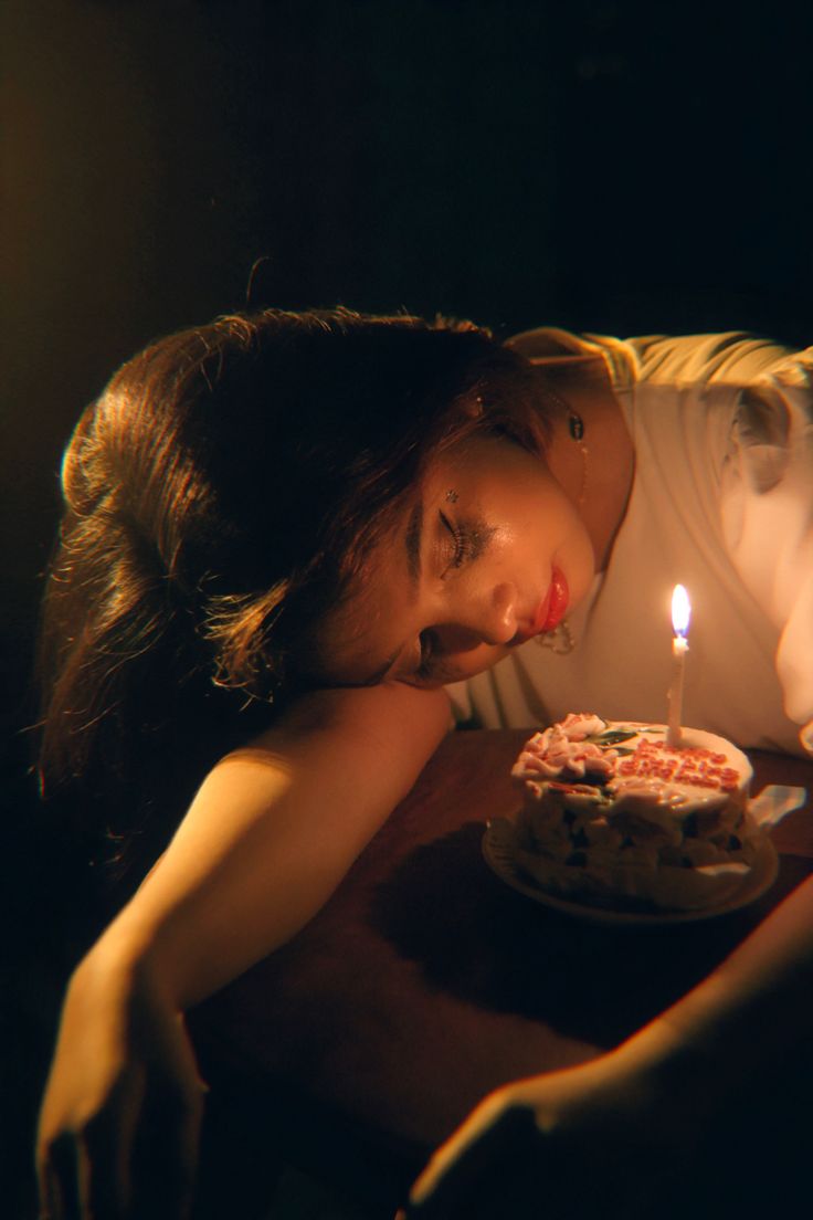 a woman laying her head on a table with a birthday cake