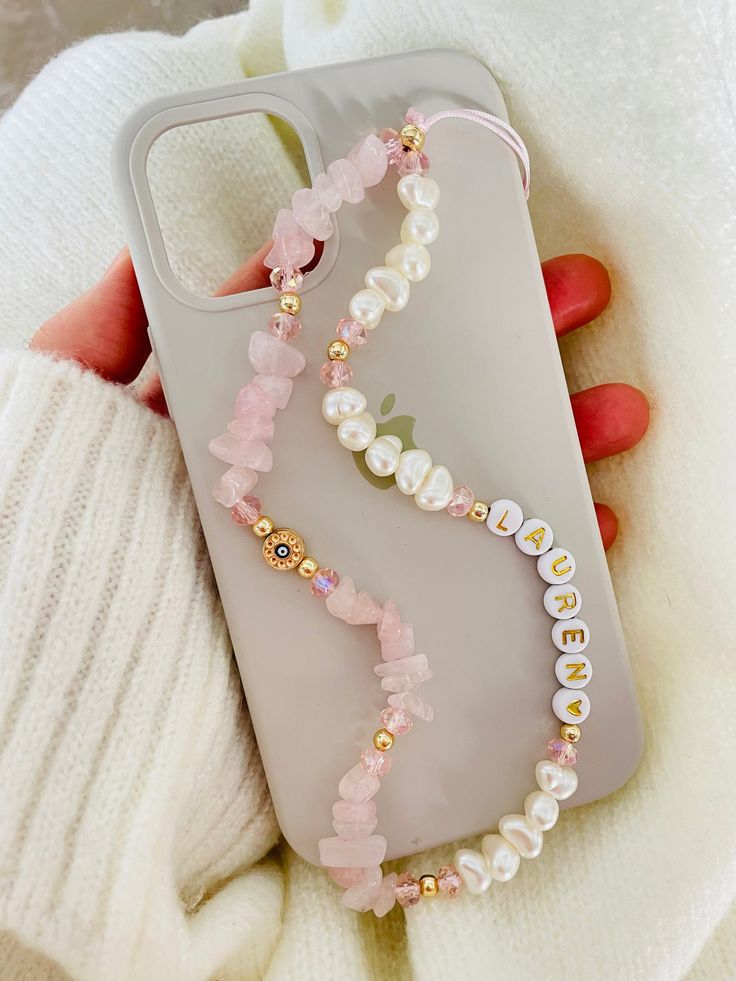 a person holding a phone case with pearls and beads on it