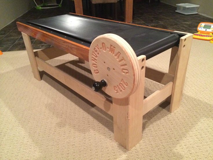 a wooden table with a black top and wheels attached to the legs, sitting on carpeted flooring