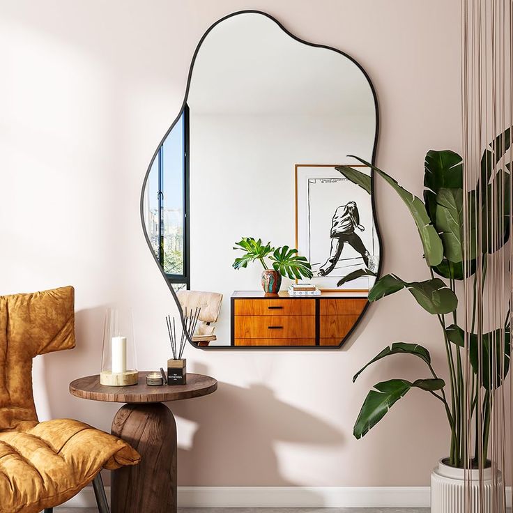 a mirror hanging on the wall next to a table with a chair and potted plant