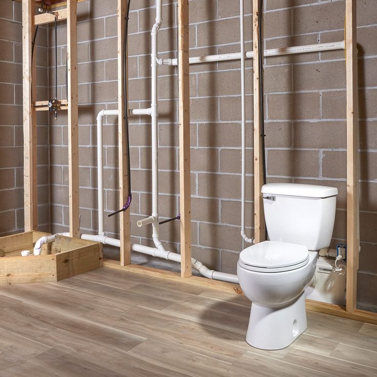 a white toilet sitting in a bathroom next to a brick wall with pipes on it