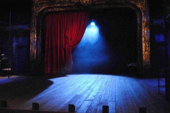 an empty stage with a red curtain and light coming from the top to the floor