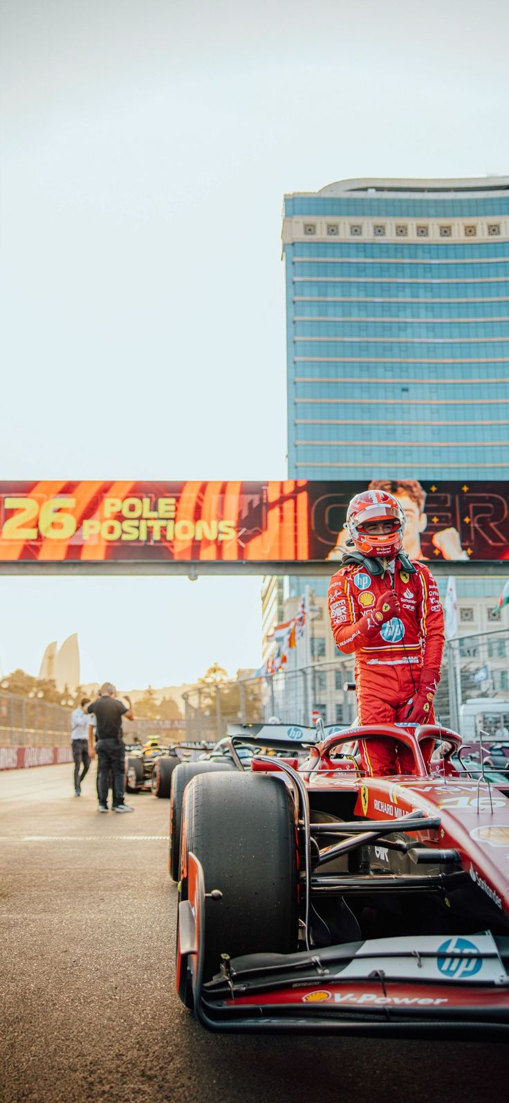 a man standing on top of a race car in front of a tall building with a sign above it