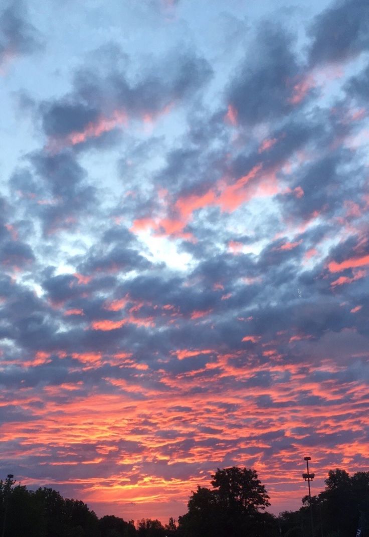 the sun is setting behind some clouds in the sky over a parking lot and trees