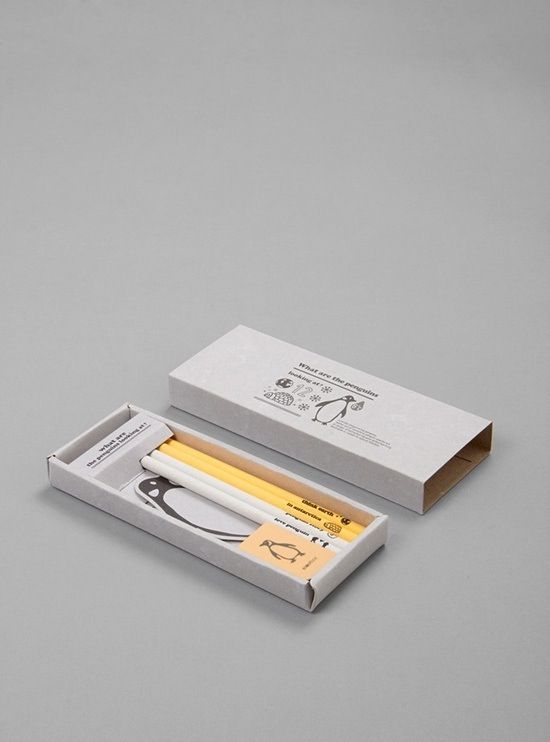 an open box with scissors and pencils inside on a gray surface next to a pair of scissors